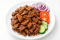 Plated dish of grilled suya meat with sliced tomatoes, cucumbers, and onions on a white background